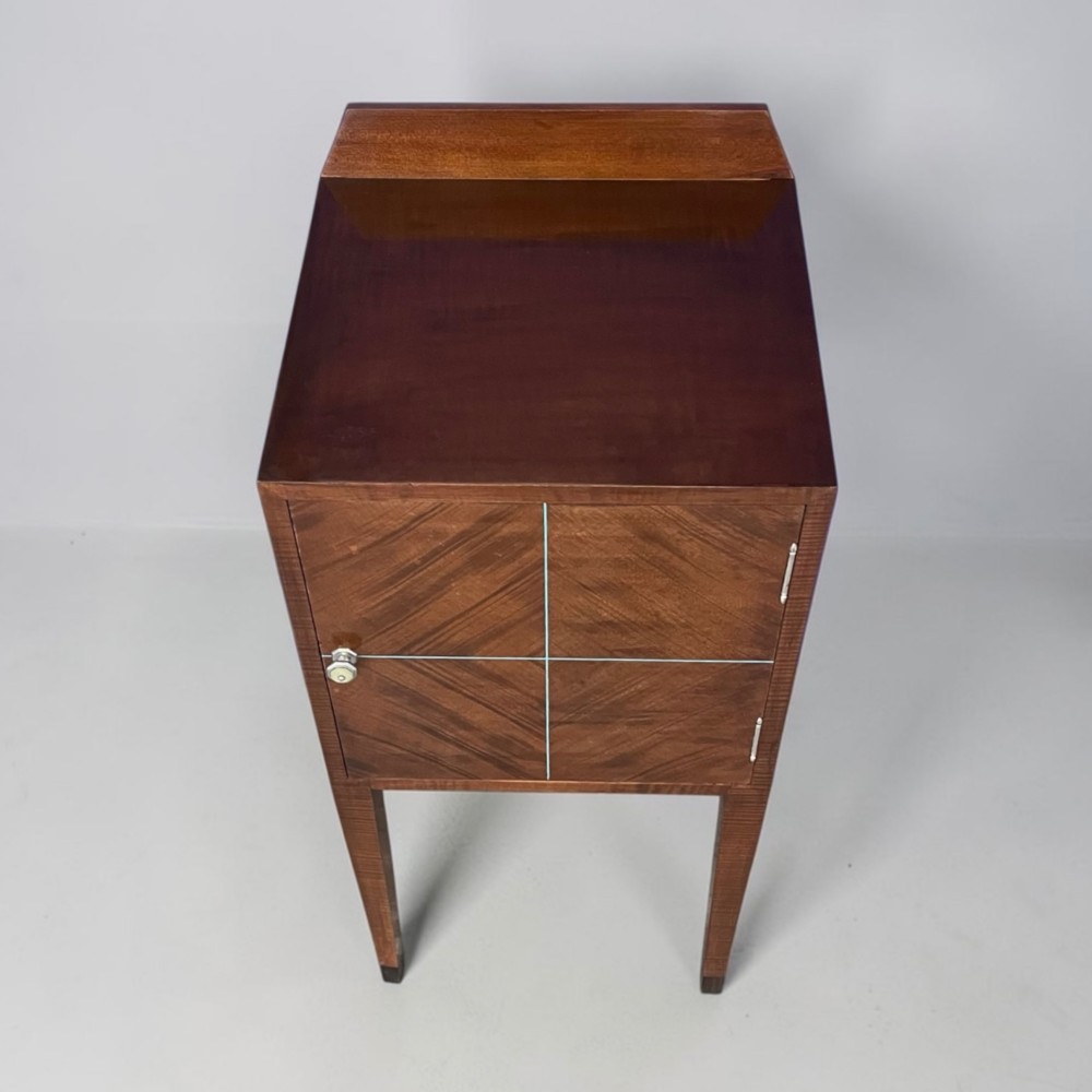 An Art Deco figured walnut bedside table featuring a raised gallery back, geometric parquetry double doors, and slender tapered legs. View V