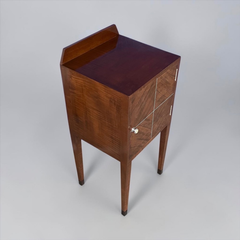 An Art Deco figured walnut bedside table featuring a raised gallery back, geometric parquetry double doors, and slender tapered legs. View VIII