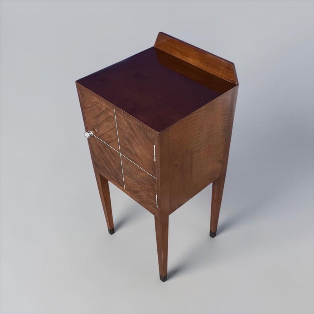 An Art Deco figured walnut bedside table featuring a raised gallery back, geometric parquetry double doors, and slender tapered legs. View IX