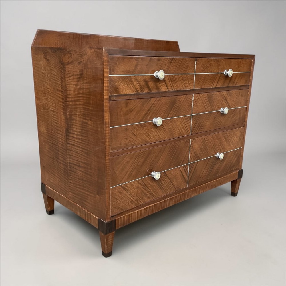 An Art Deco figured walnut chest of drawers featuring three long drawers with chevron veneer patterning, octagonal handles, inlaid horizontal lines, and tapered feet.