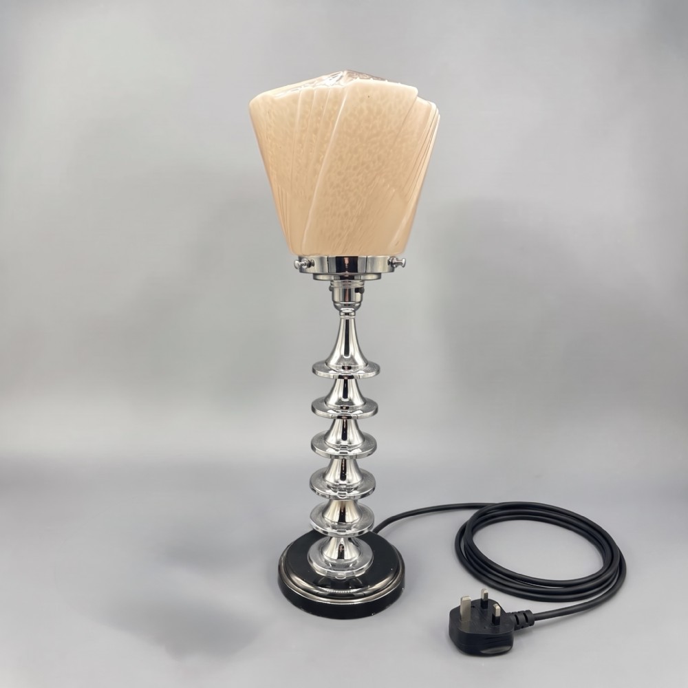 An Art Deco table lamp featuring a stepped chrome column stem and a cream fan-shaped moulded glass shade.