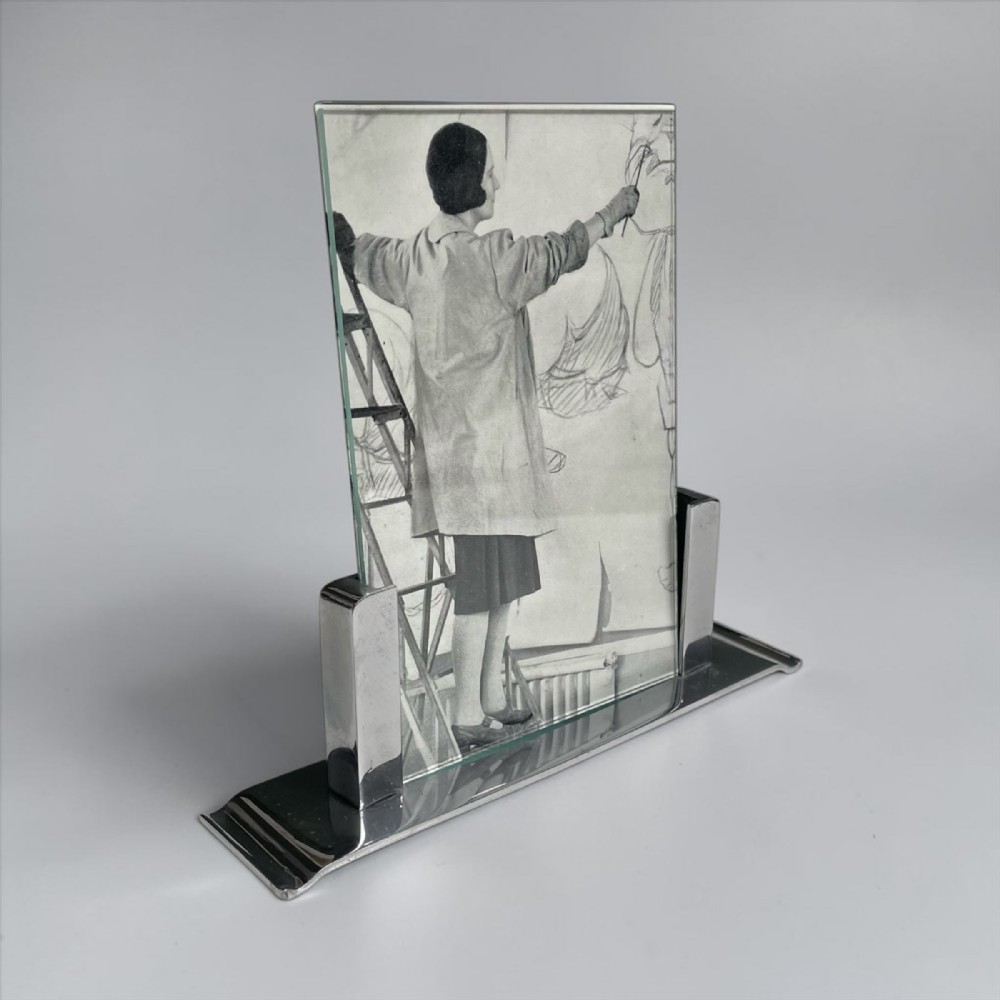 An Art Deco chrome and glass picture frame featuring a geometric stepped base holding a vertical glass sheet.