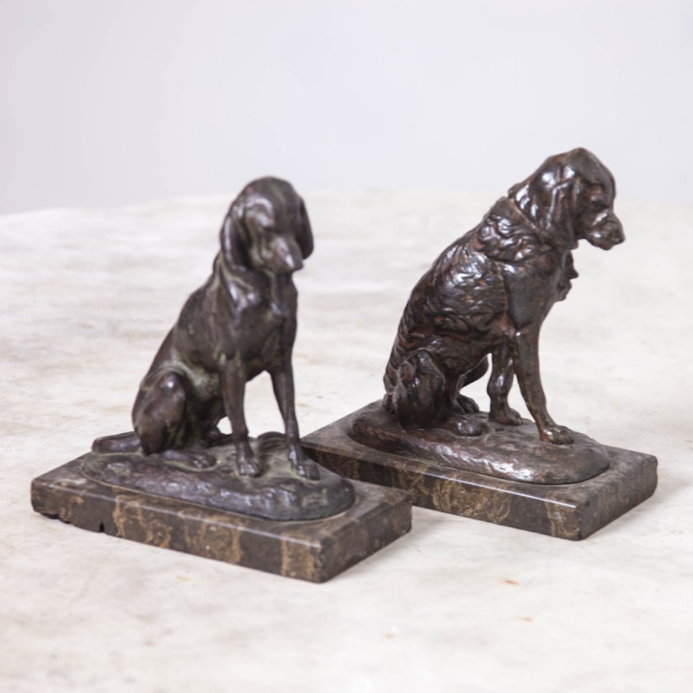A pair of patinated cast metal figures depicting seated dogs mounted on rectangular dark marble plinths. View III