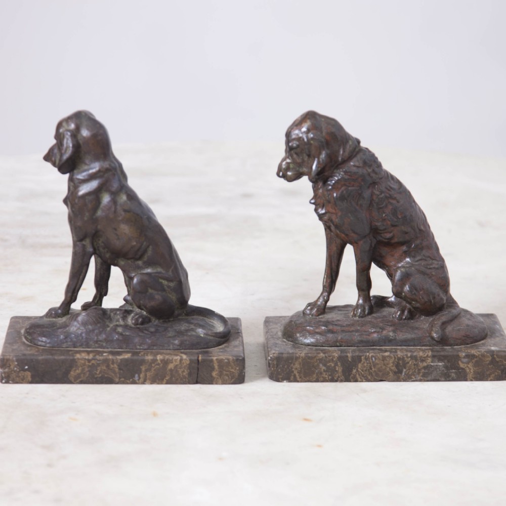 A pair of patinated cast metal figures depicting seated dogs mounted on rectangular dark marble plinths. View IV
