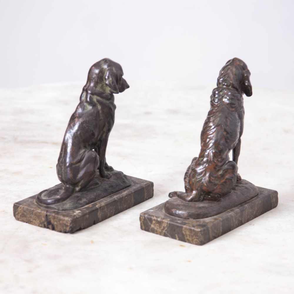 A pair of patinated cast metal figures depicting seated dogs mounted on rectangular dark marble plinths. View V