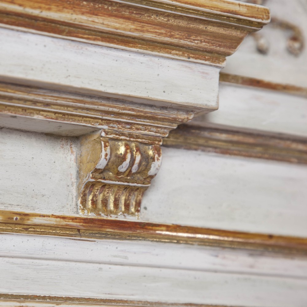 A matching pair of Neoclassical wall mirrors featuring cream painted frames with gilded pediments, scroll cresting, and rectangular mirror glass. View IV