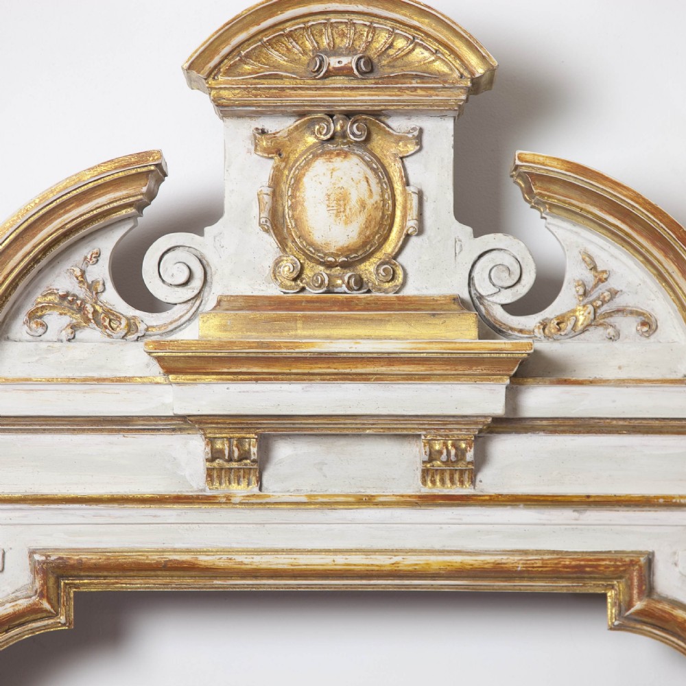 A matching pair of Neoclassical wall mirrors featuring cream painted frames with gilded pediments, scroll cresting, and rectangular mirror glass. View V