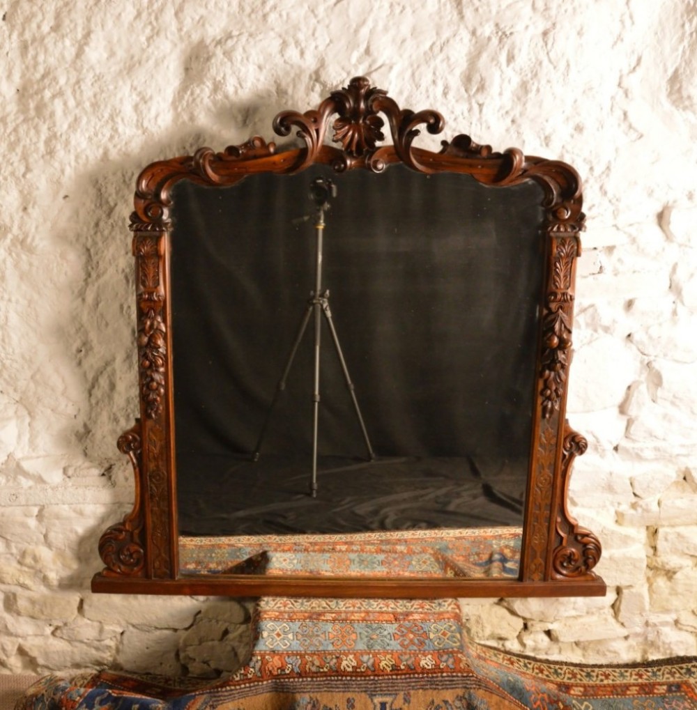 A Victorian dark mahogany overmantel mirror featuring an arched frame topped with a carved acanthus cresting and carved floral side details.