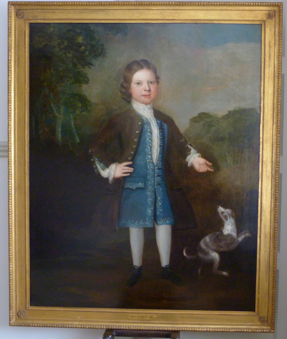 An early 18th-century oil painting depicting a standing boy in a brown coat and blue waistcoat alongside a small dog, presented in a beaded giltwood frame.
