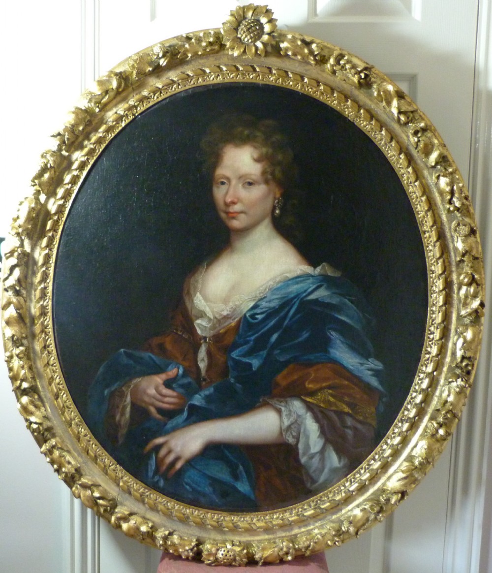An oval 17th-century oil painting depicting a noblewoman dressed in a blue drape and lace-trimmed gown within an ornate carved giltwood frame.