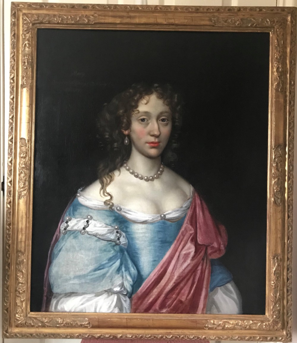 An antique seventeenth-century oil portrait of a noblewoman in a blue dress and pearl jewellery set within an ornate carved giltwood frame.