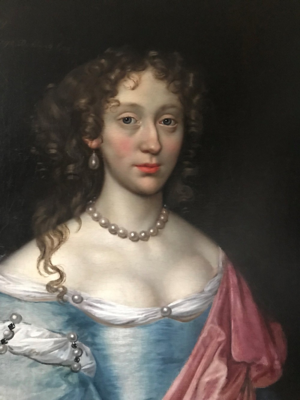 An antique seventeenth-century oil portrait of a noblewoman in a blue dress and pearl jewellery set within an ornate carved giltwood frame. View II