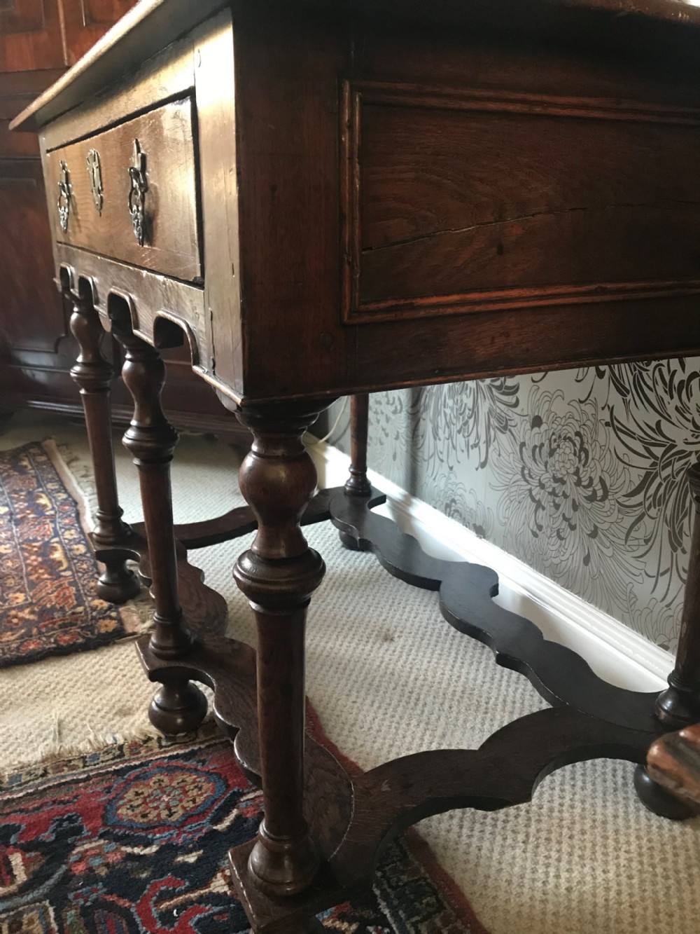 A dark oak side table with a single drawer featuring brass drop handles, a shaped apron, turned baluster legs, and a wavy stretcher base. View IV