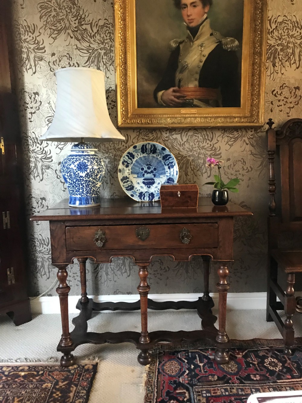 A dark oak side table with a single drawer featuring brass drop handles, a shaped apron, turned baluster legs, and a wavy stretcher base. View VI