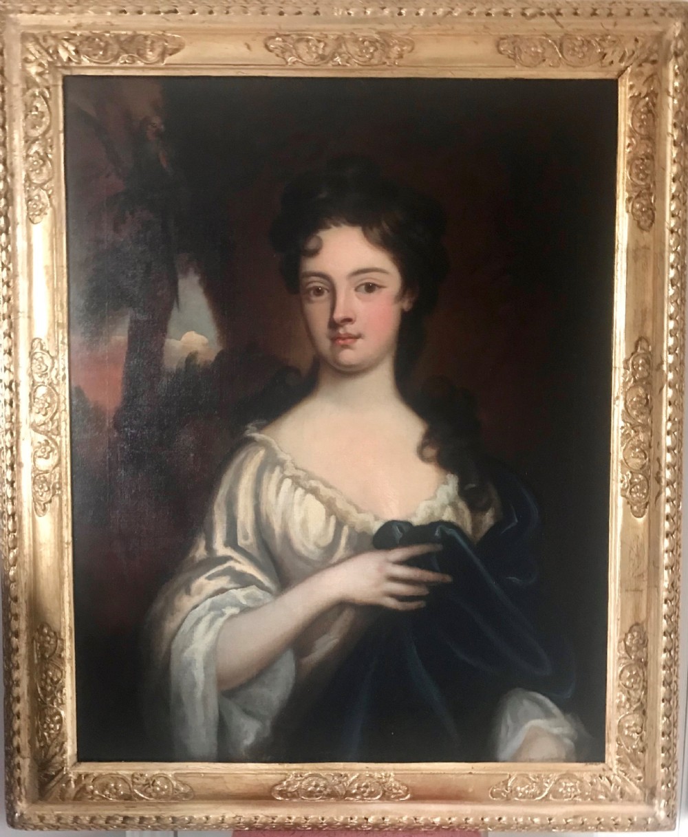 An 18th-century oil portrait painting of a woman in a white gown with a blue drape, set within a carved gold gilt frame.