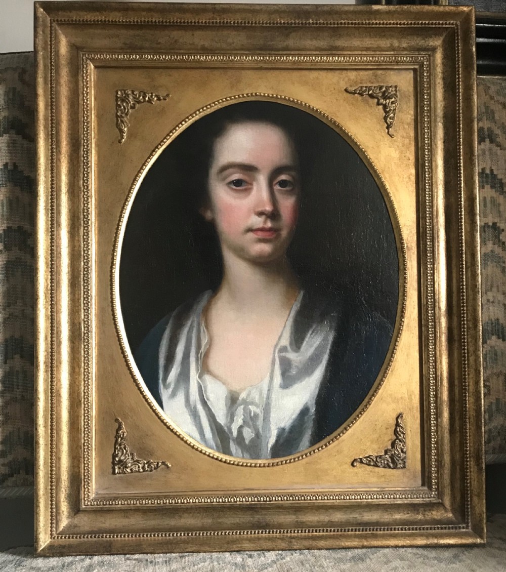 An 18th-century oil portrait of a lady in a white gown and blue mantle, framed by a feigned oval inside an ornate gold rectangular frame.