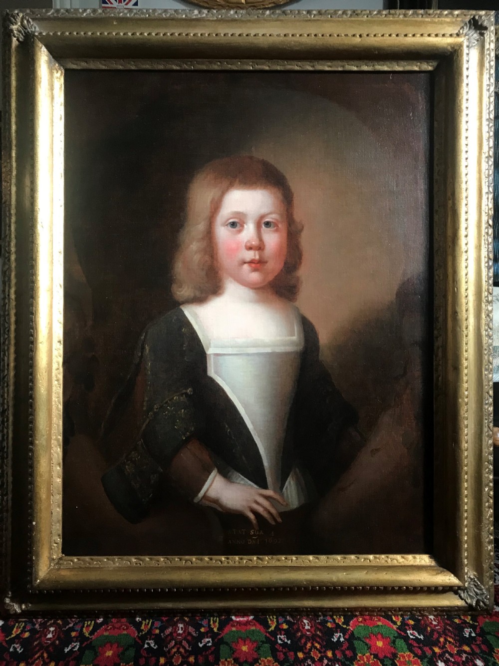 An antique seventeenth-century oil portrait of a young boy with light brown hair in period dress, set in a carved gilt frame.