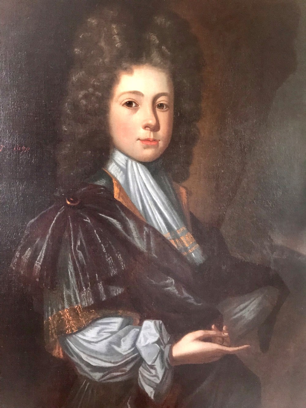An early 18th-century oil portrait depicting a young male with long dark curled hair, a light blue cravat, and a dark draped cloak against a dark background. View II