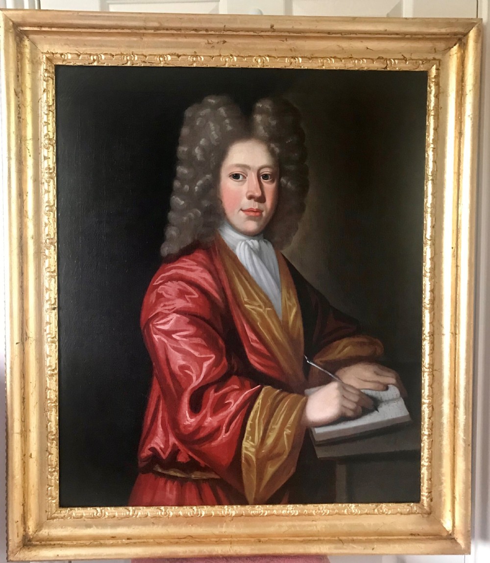 An early 18th-century oil painting on canvas depicting a gentleman in a full wig and red silk robe writing in a book, presented within a gilded frame.