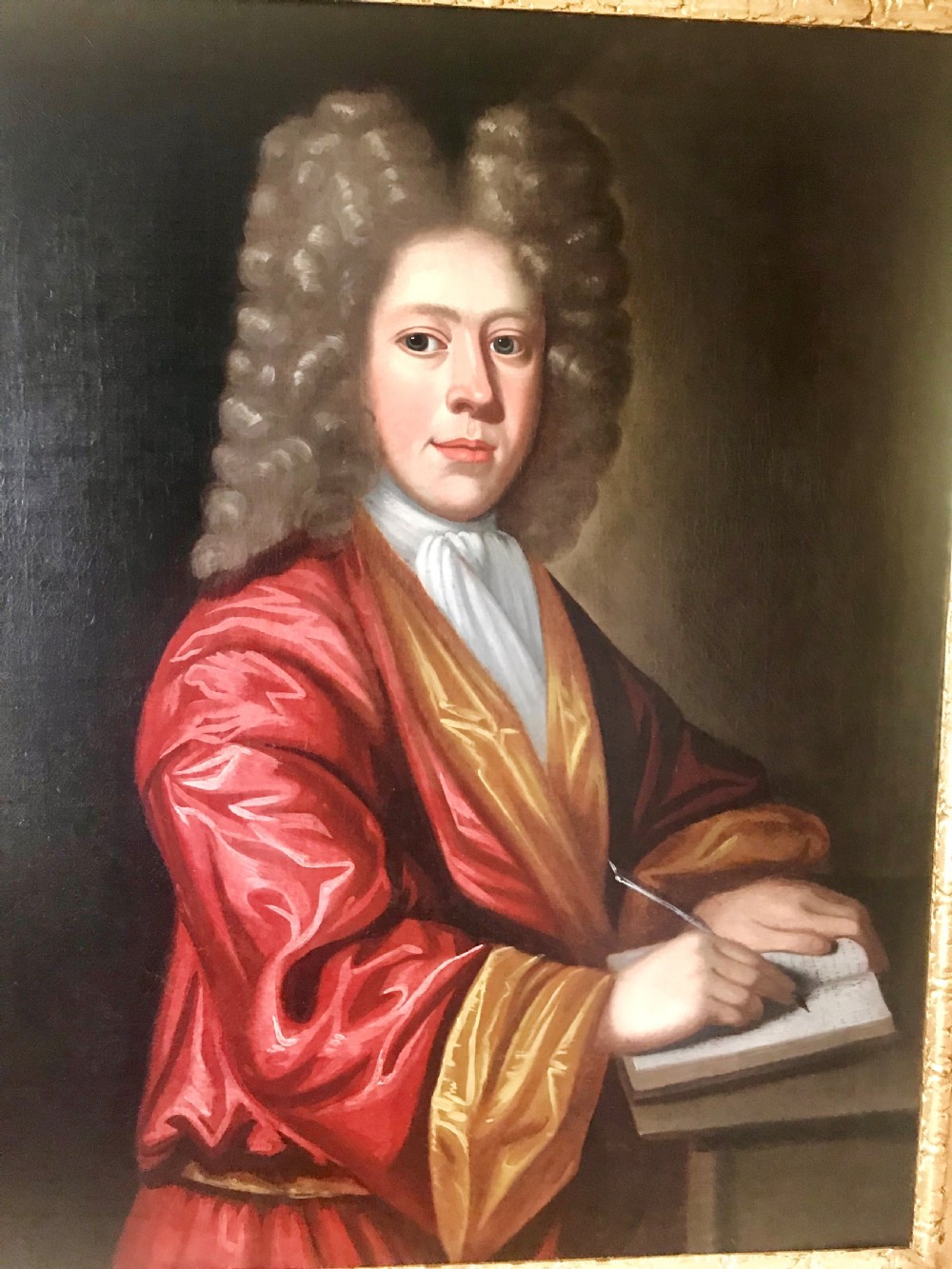 An early 18th-century oil painting on canvas depicting a gentleman in a full wig and red silk robe writing in a book, presented within a gilded frame. View II