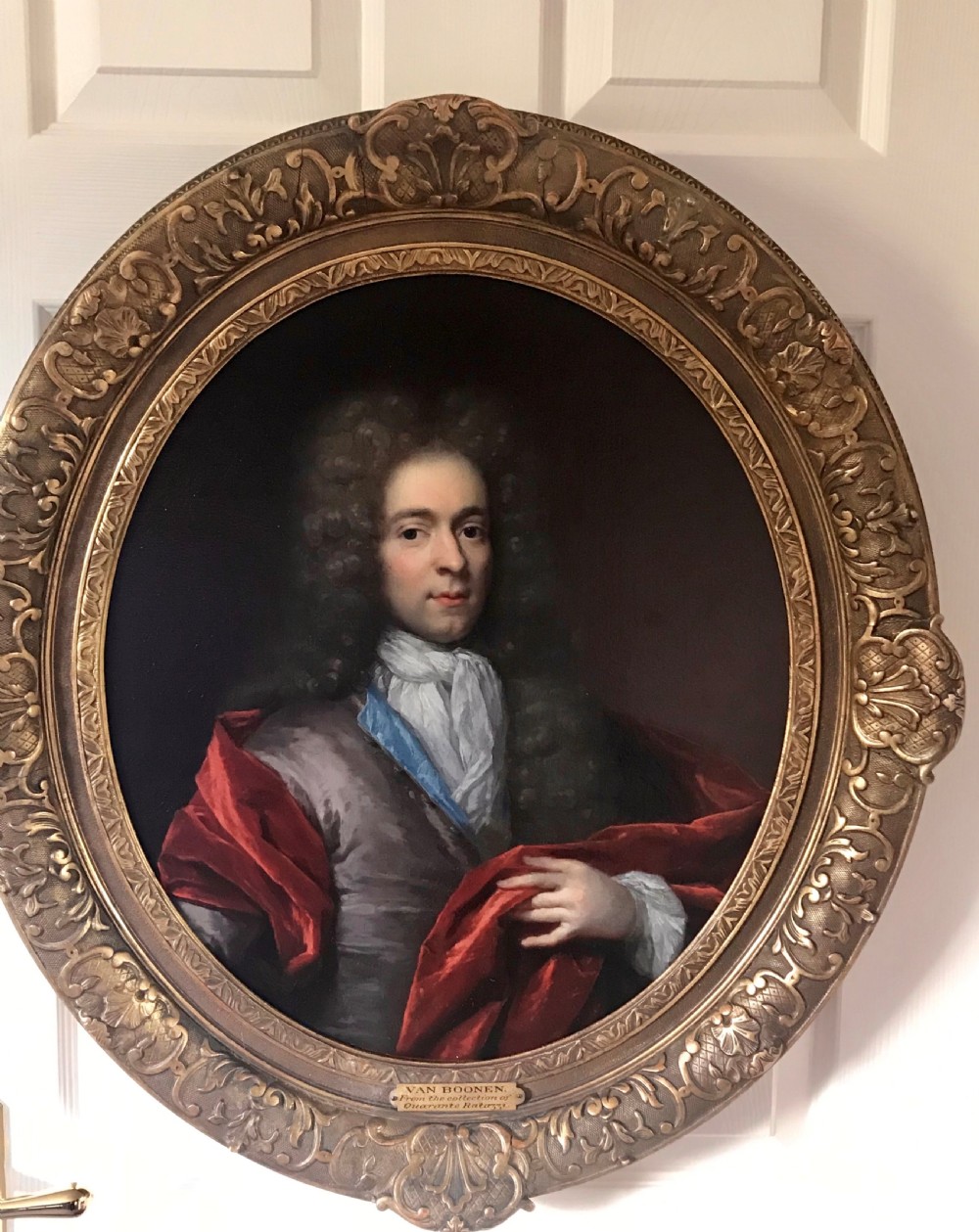 An oval seventeenth-century oil painting depicting a gentleman wearing a periwig and crimson cloak, set inside a carved giltwood frame.