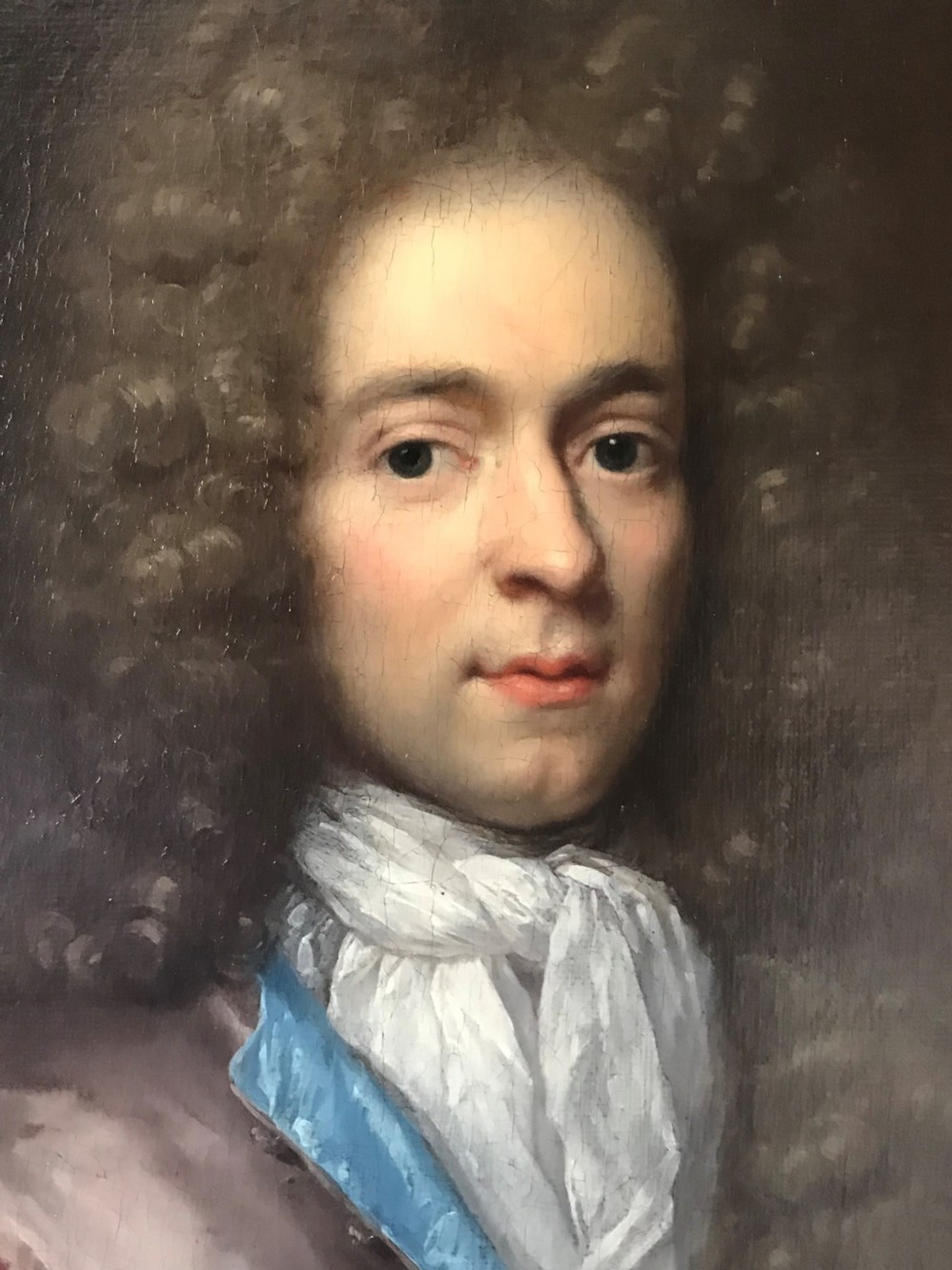 An oval seventeenth-century oil painting depicting a gentleman wearing a periwig and crimson cloak, set inside a carved giltwood frame. View III