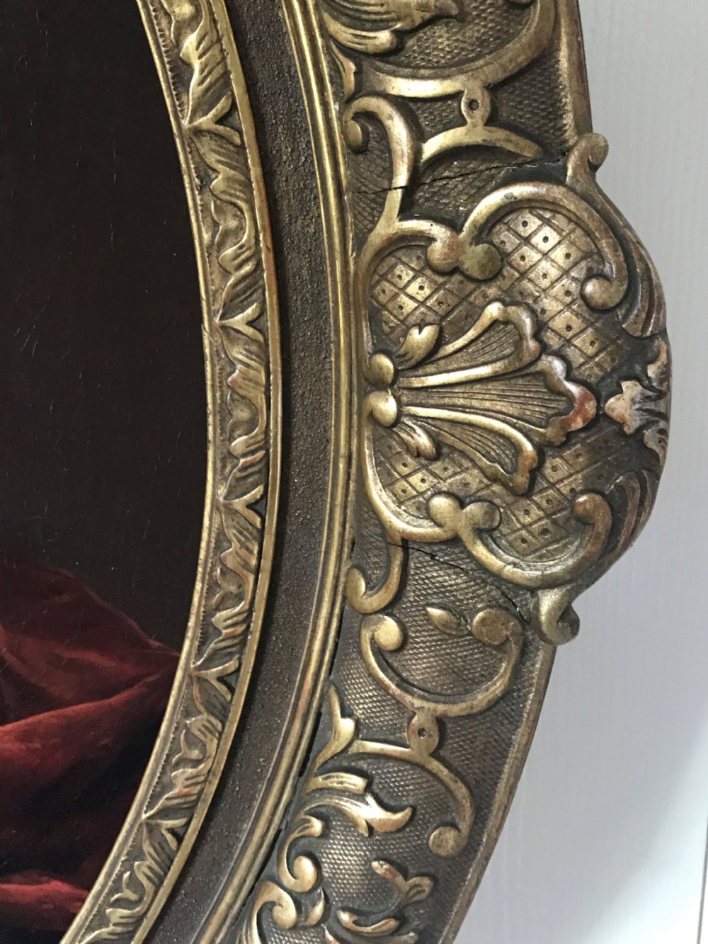 An oval seventeenth-century oil painting depicting a gentleman wearing a periwig and crimson cloak, set inside a carved giltwood frame. View V