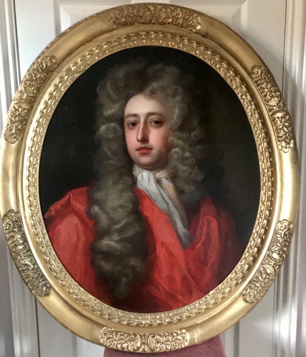 An oval oil portrait of a gentleman in a long powdered wig and red drapery, housed within a carved giltwood frame.