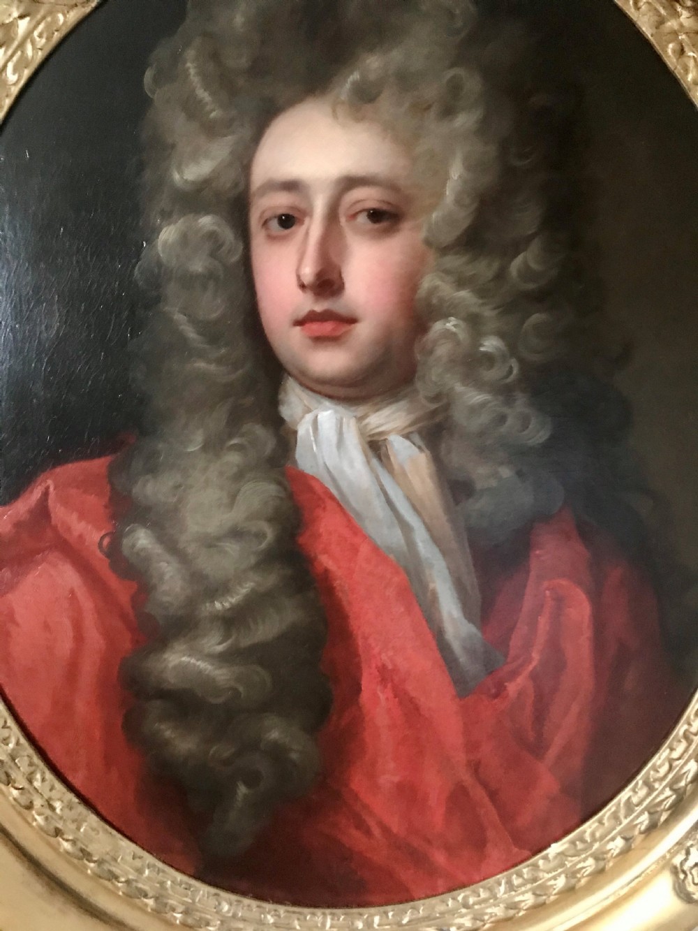 An oval oil portrait of a gentleman in a long powdered wig and red drapery, housed within a carved giltwood frame. View II