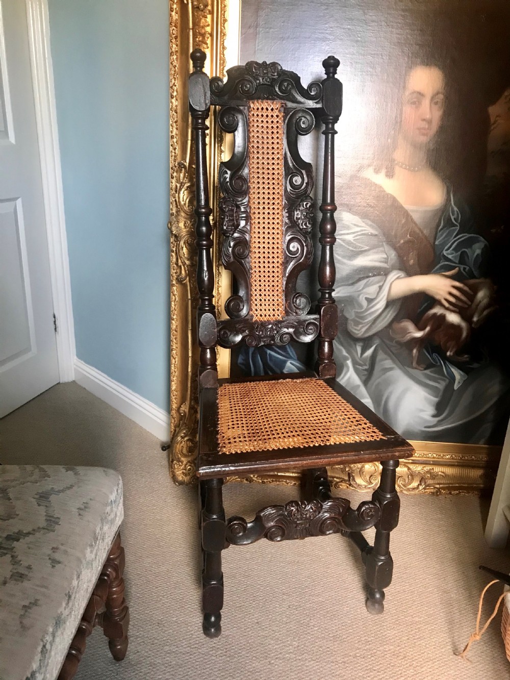 A late 17th-century dark carved beech side chair featuring a tall back with scrollwork, turned supports, and woven cane panels.