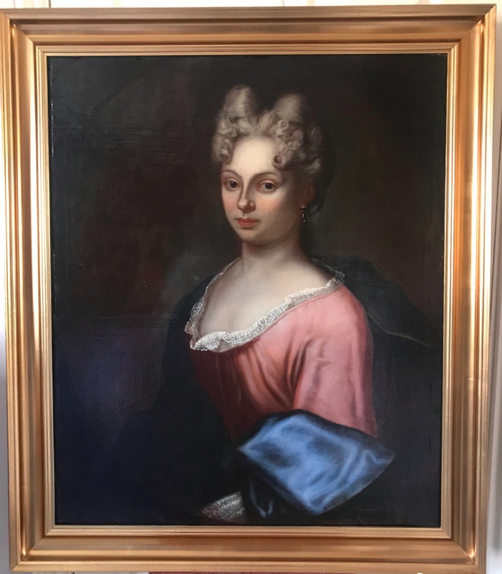 An 18th-century oil painting depicting a woman in a pink gown with lace trimming, set in a gilded wooden frame.