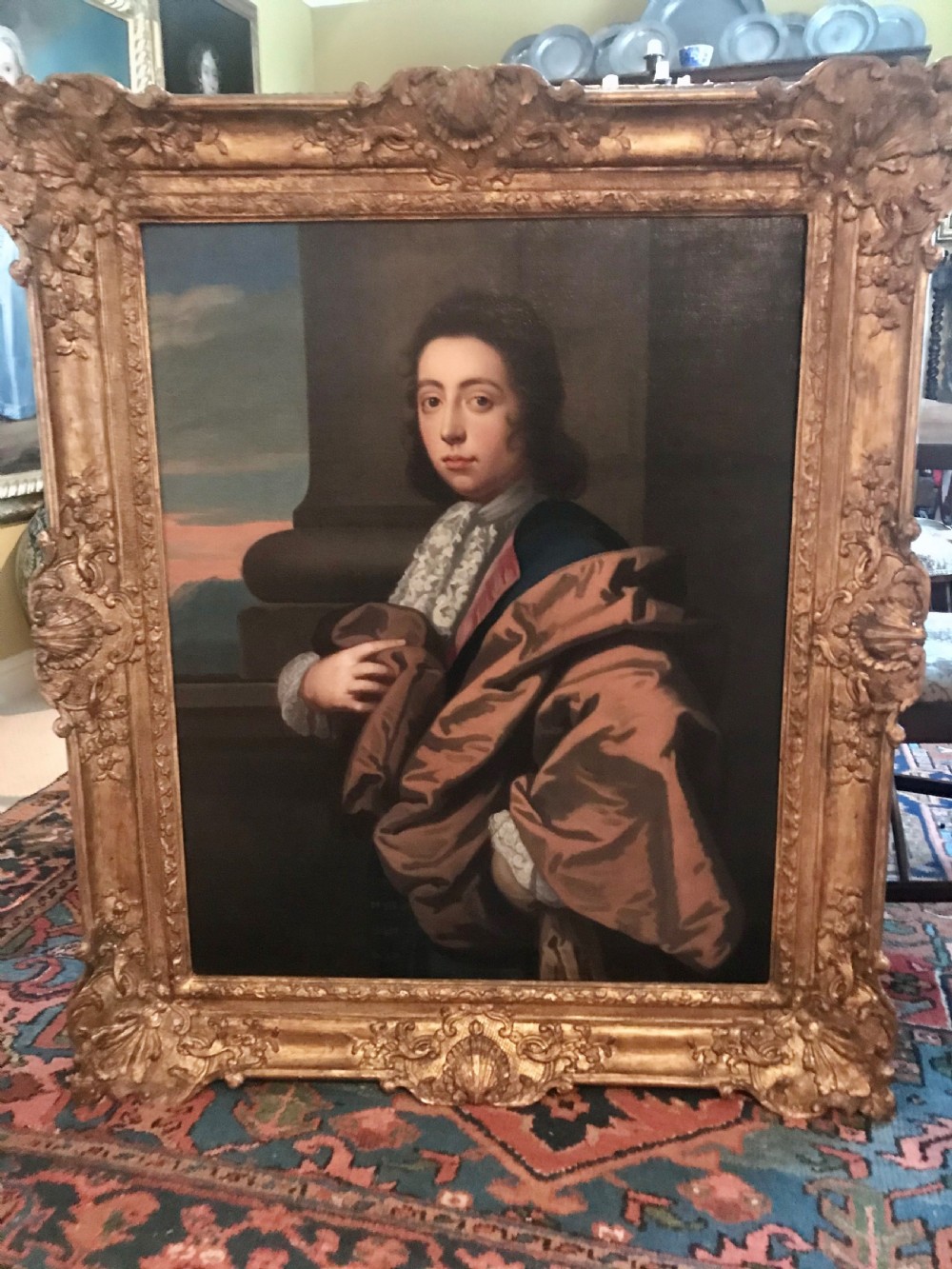 A seventeenth-century oil painting depicting a young gentleman in brown drapery and lace cravat set in a deeply carved giltwood frame.