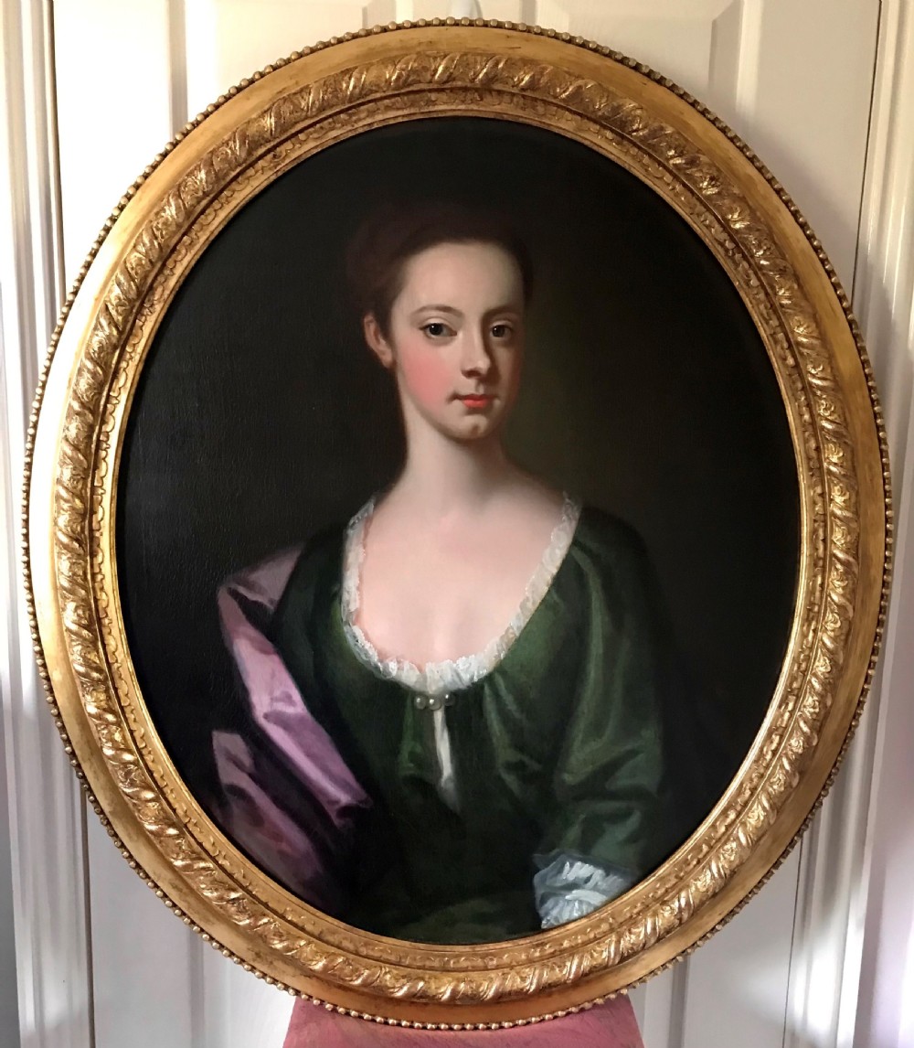 An 18th-century oval oil portrait on canvas depicting a lady in a green dress and purple mantle within a carved gilded frame.