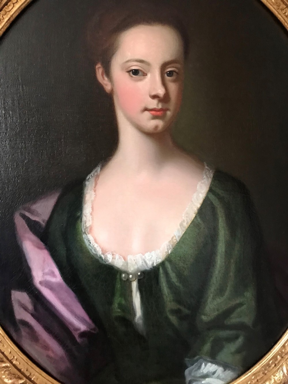 An 18th-century oval oil portrait on canvas depicting a lady in a green dress and purple mantle within a carved gilded frame. View II