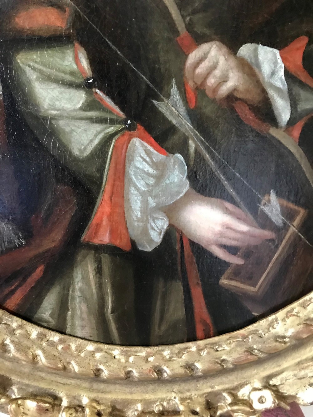 An oval Baroque oil painting depicting a young boy holding a bow, set within an ornate carved giltwood frame. View III