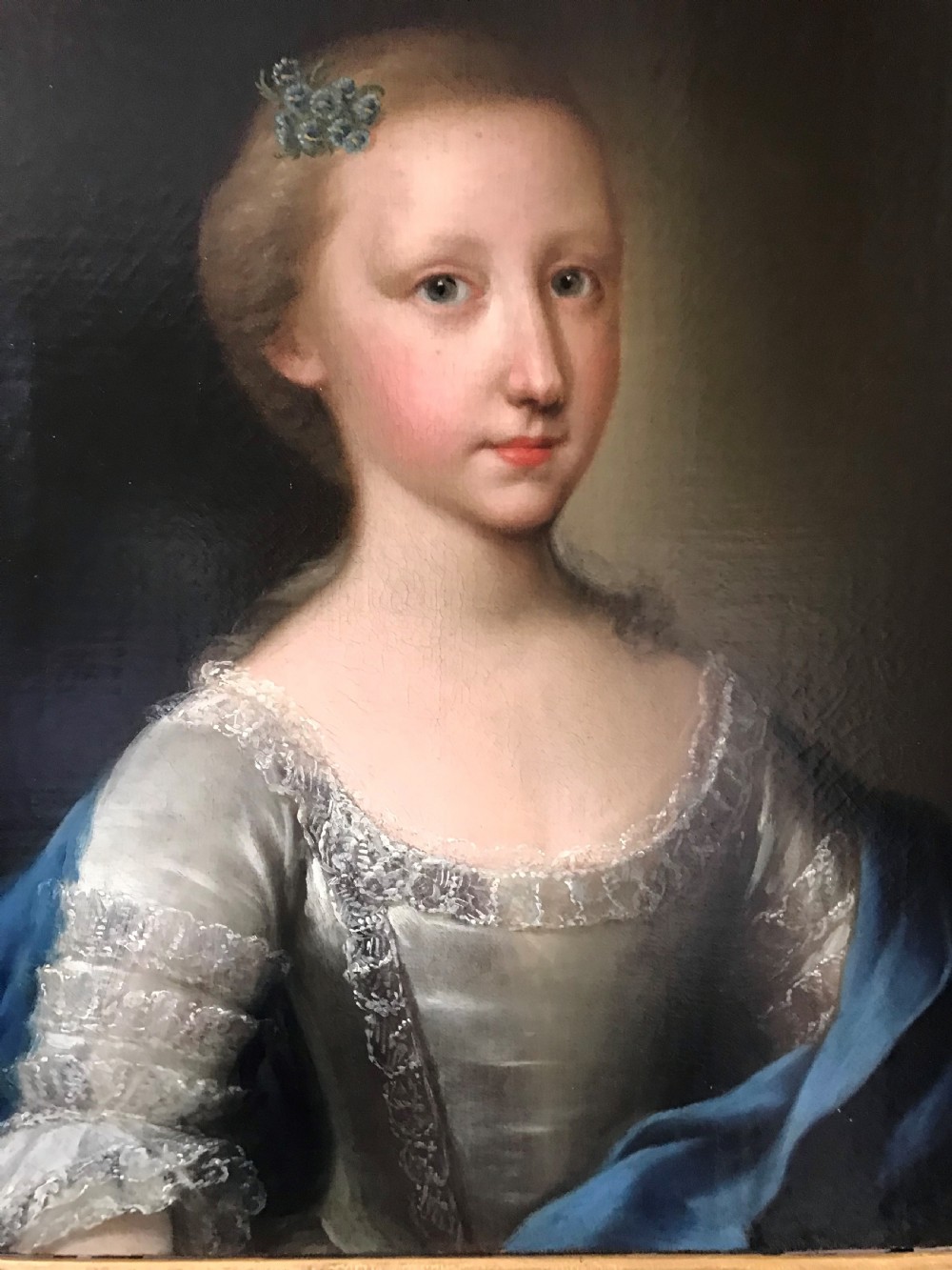 An 18th-century oil portrait depicting a young girl in a lace-trimmed dress and blue shawl, presented within a carved giltwood frame. View II