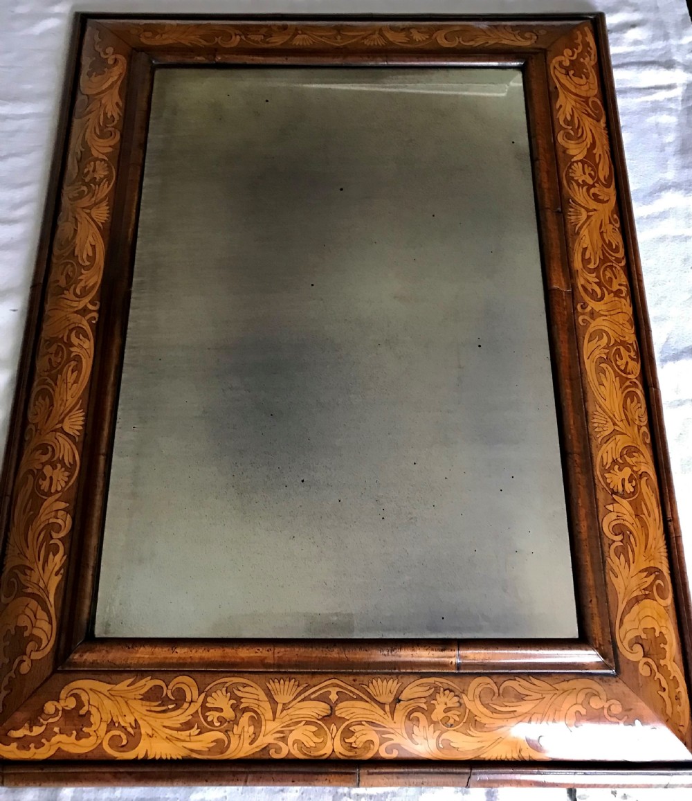 A rectangular William and Mary period wall mirror featuring a broad wooden cushion frame decorated with intricate floral marquetry inlays.