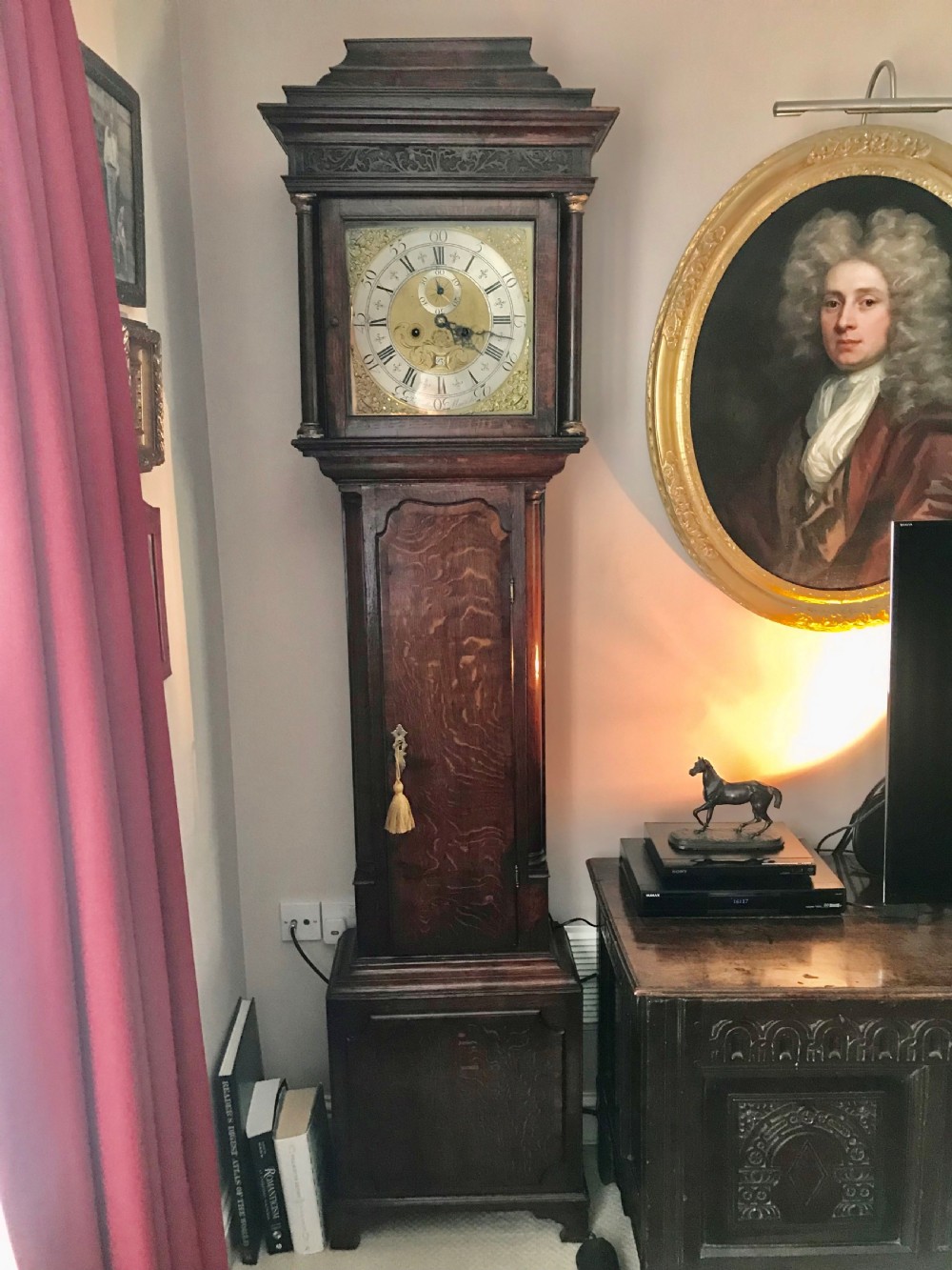 An 18th-century dark oak longcase clock featuring a square brass dial, moulded hood, and a shaped door on the main body.