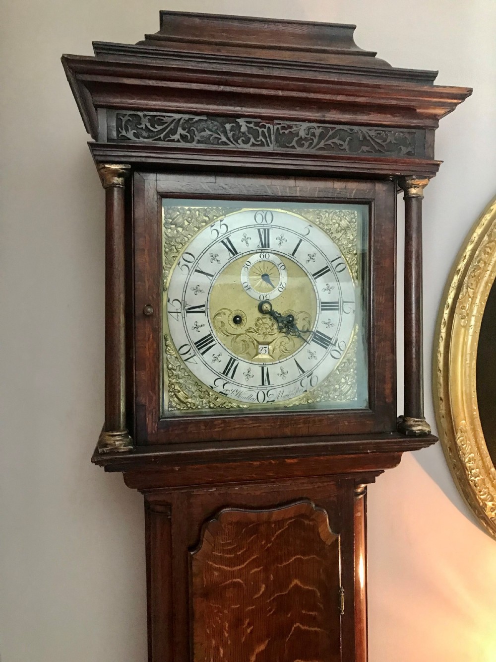 An 18th-century dark oak longcase clock featuring a square brass dial, moulded hood, and a shaped door on the main body. View V