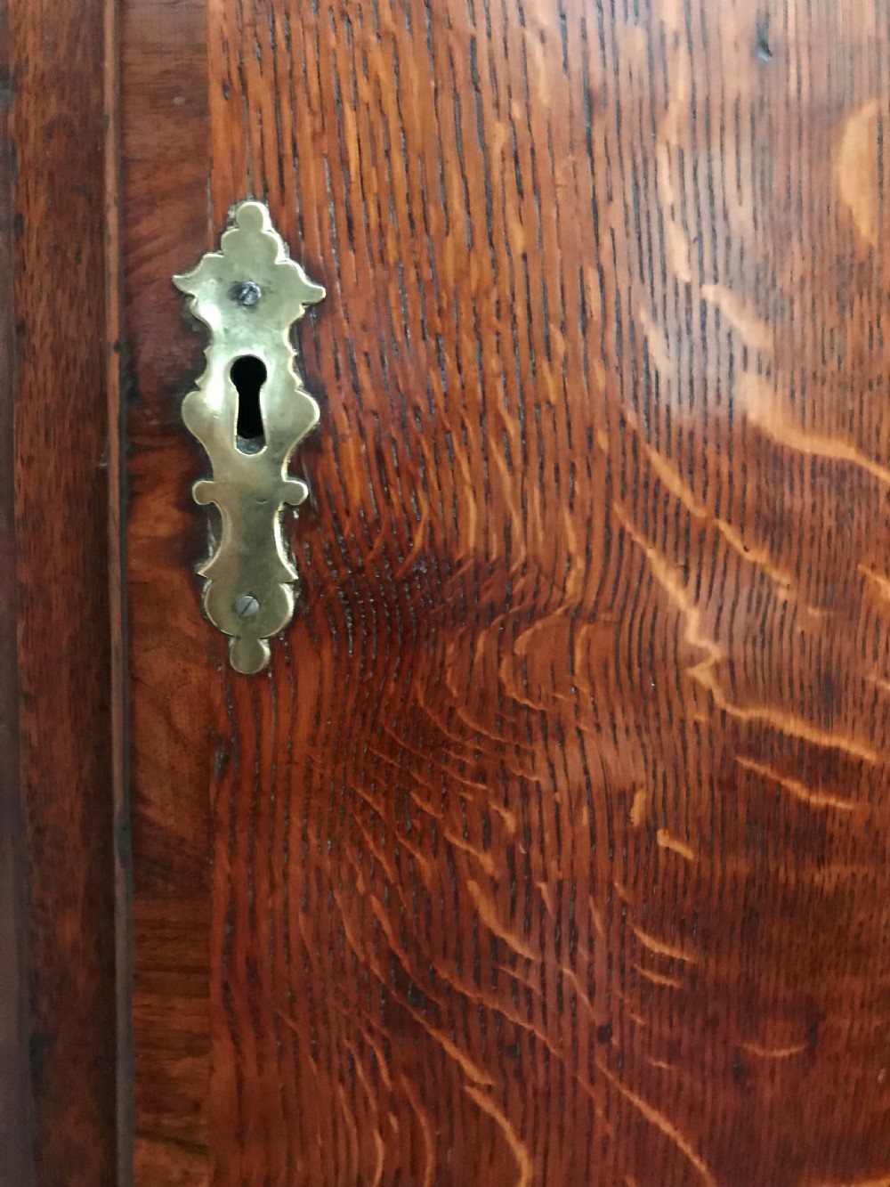 An 18th-century dark oak longcase clock featuring a square brass dial, moulded hood, and a shaped door on the main body. View VI