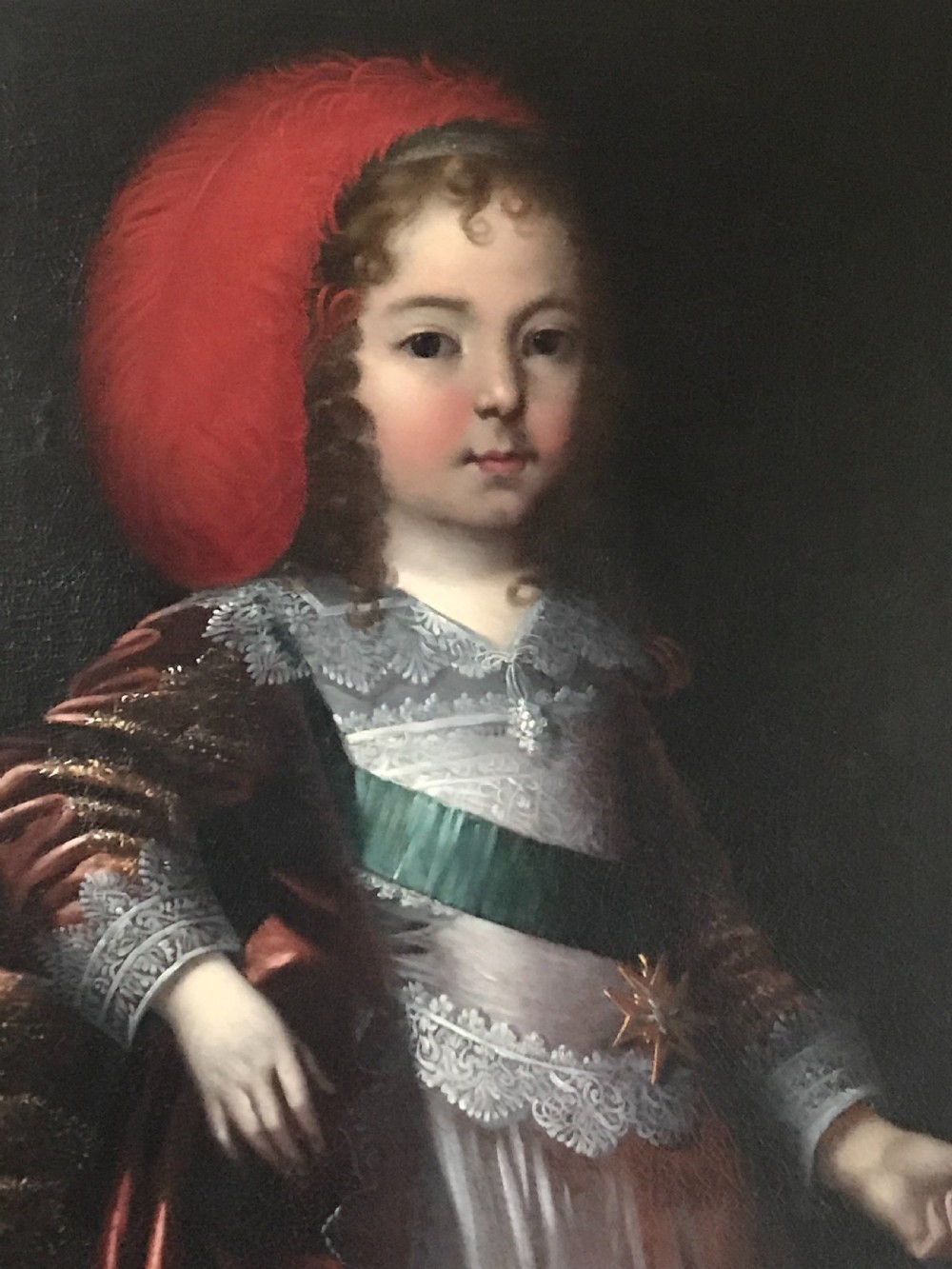 A seventeenth-century Baroque oil painting on canvas depicting a young child wearing a crimson feathered hat and ornate lace attire within a gilded wood frame. View II