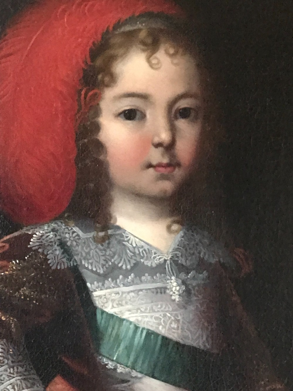 A seventeenth-century Baroque oil painting on canvas depicting a young child wearing a crimson feathered hat and ornate lace attire within a gilded wood frame. View III
