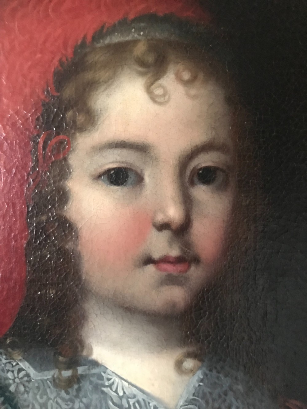 A seventeenth-century Baroque oil painting on canvas depicting a young child wearing a crimson feathered hat and ornate lace attire within a gilded wood frame. View IV