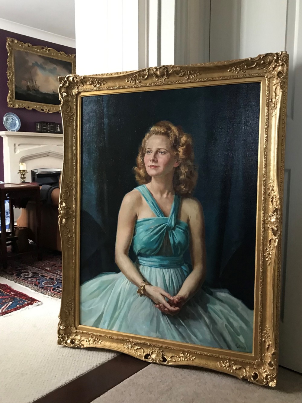 A large mid-century oil portrait depicting a woman in a blue dress, set inside an ornate carved gilt frame.