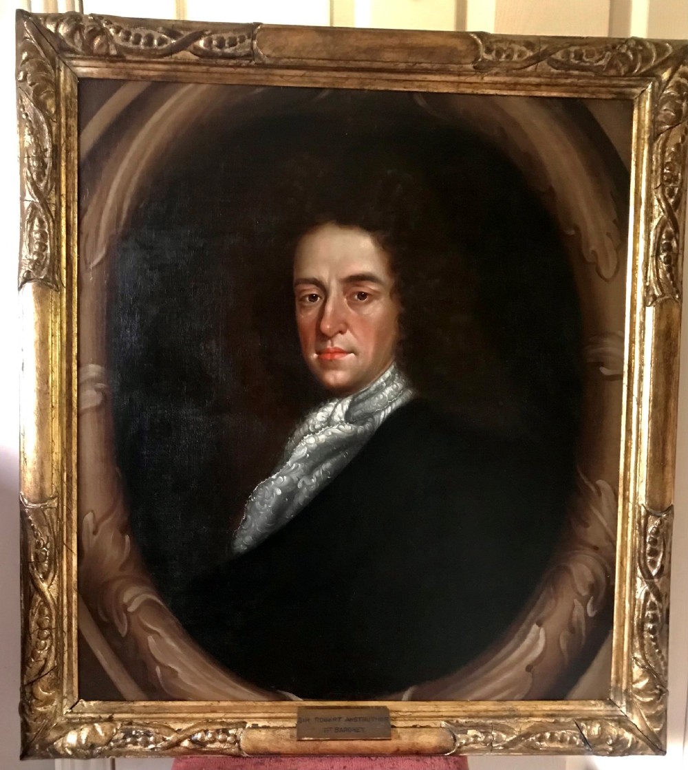 A late 17th-century Scottish oil portrait depicting a gentleman with a dark full-bottomed wig and lace cravat set within a painted feigned oval and carved gilded wooden frame.