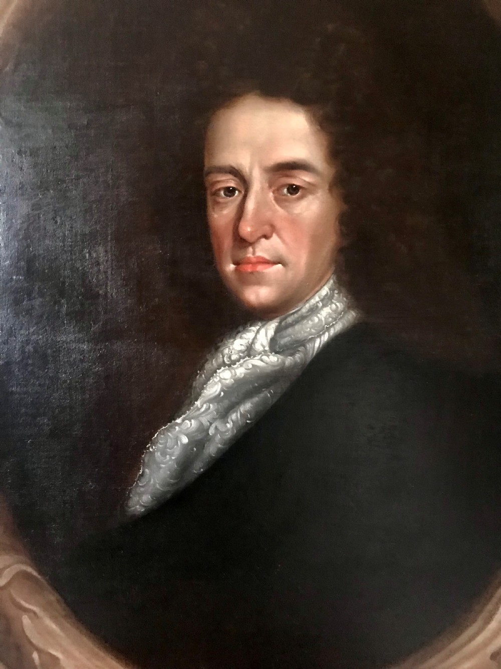 A late 17th-century Scottish oil portrait depicting a gentleman with a dark full-bottomed wig and lace cravat set within a painted feigned oval and carved gilded wooden frame. View II
