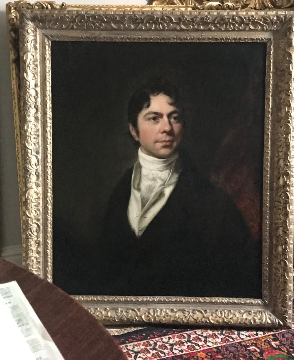 A Georgian oil portrait depicting a gentleman in a dark coat and white cravat, set within an ornate carved gilt frame.