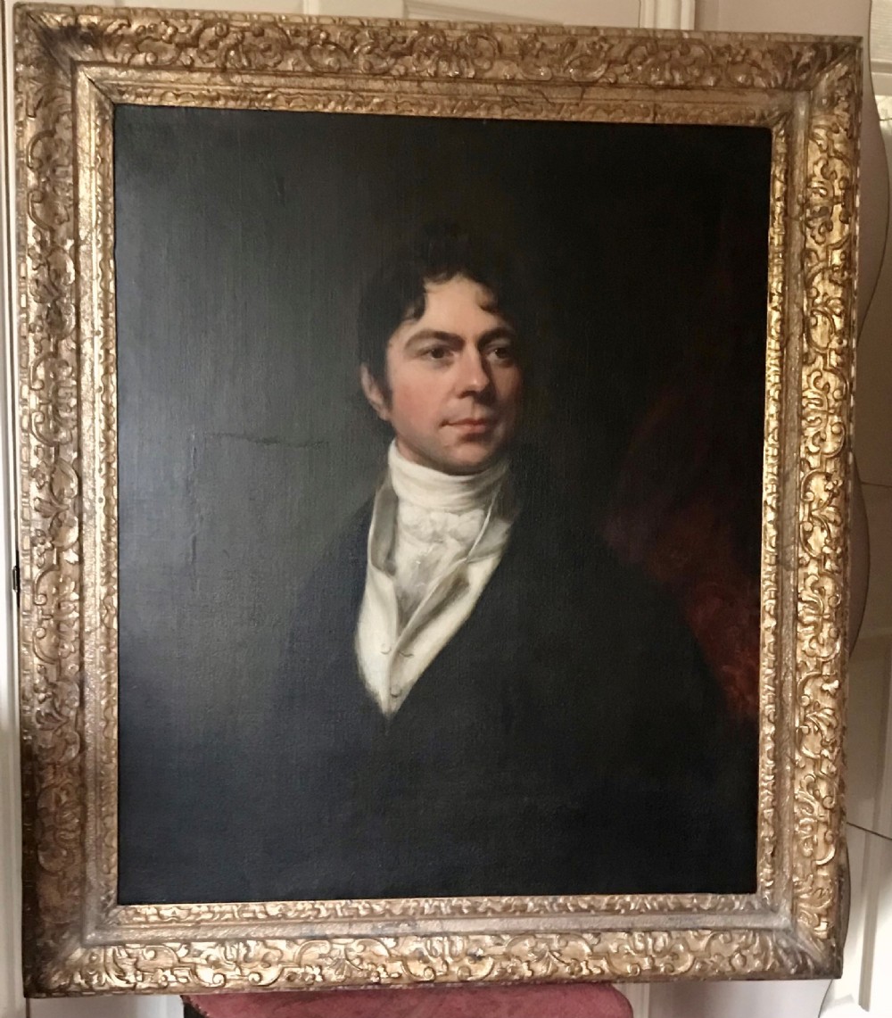 A Georgian oil portrait depicting a gentleman in a dark coat and white cravat, set within an ornate carved gilt frame. View VI