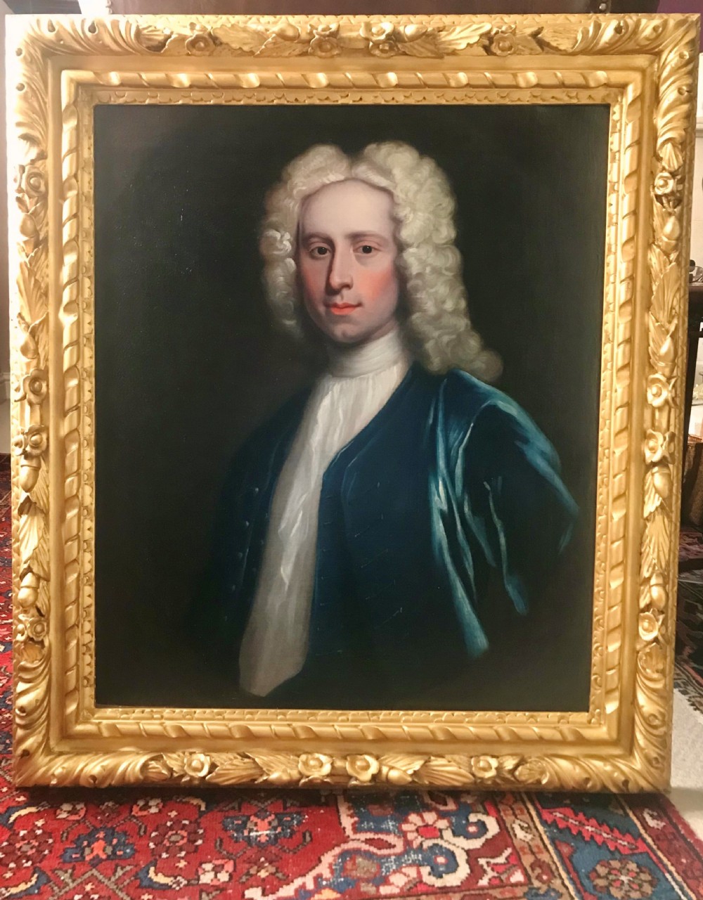 An 18th-century oil portrait depicting a gentleman wearing a powdered wig and blue coat within a carved giltwood frame.