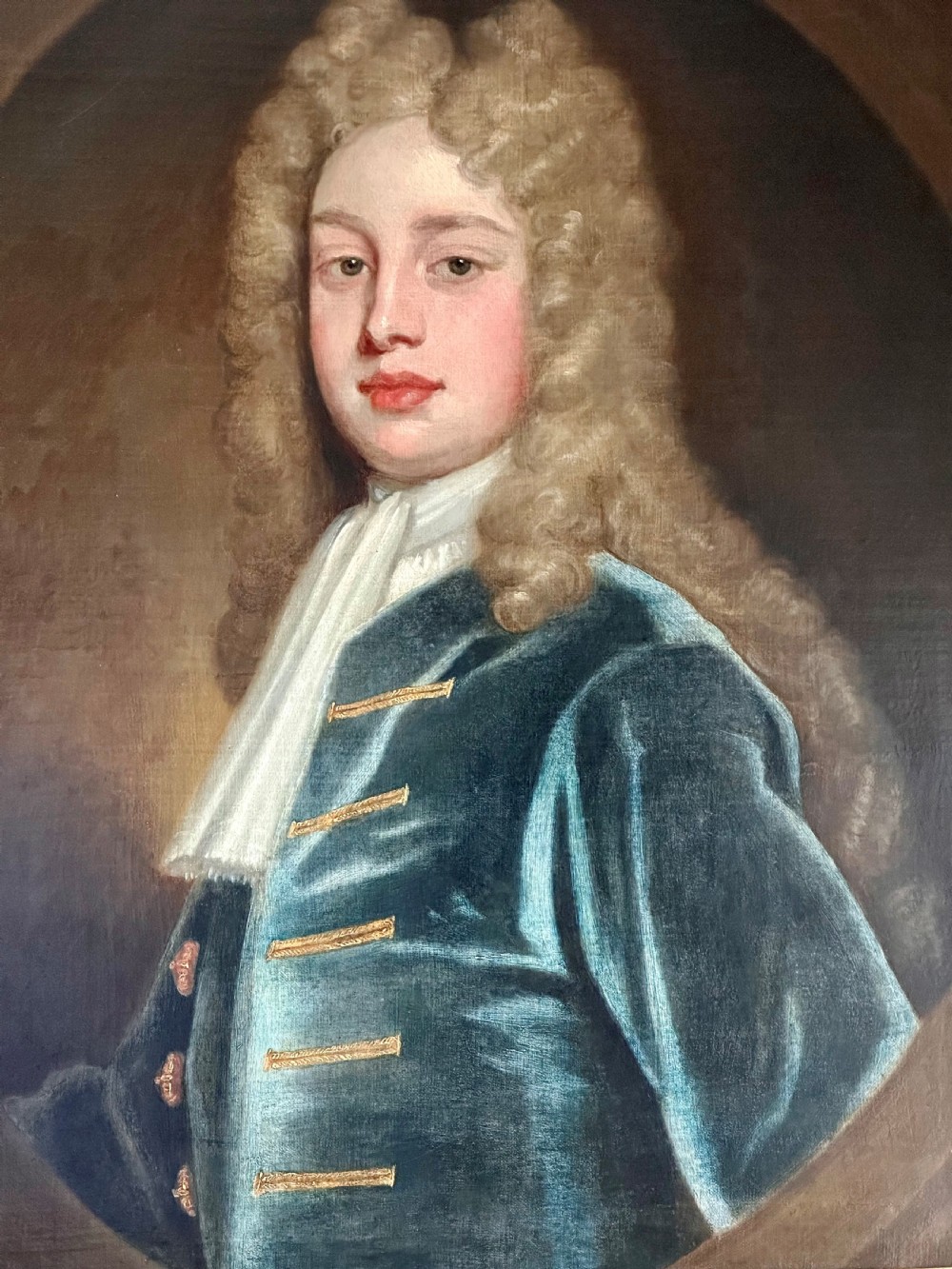 An 18th-century oil portrait painting depicting a gentleman with a long wig, white cravat, and teal blue coat, set within a carved gold frame. View II